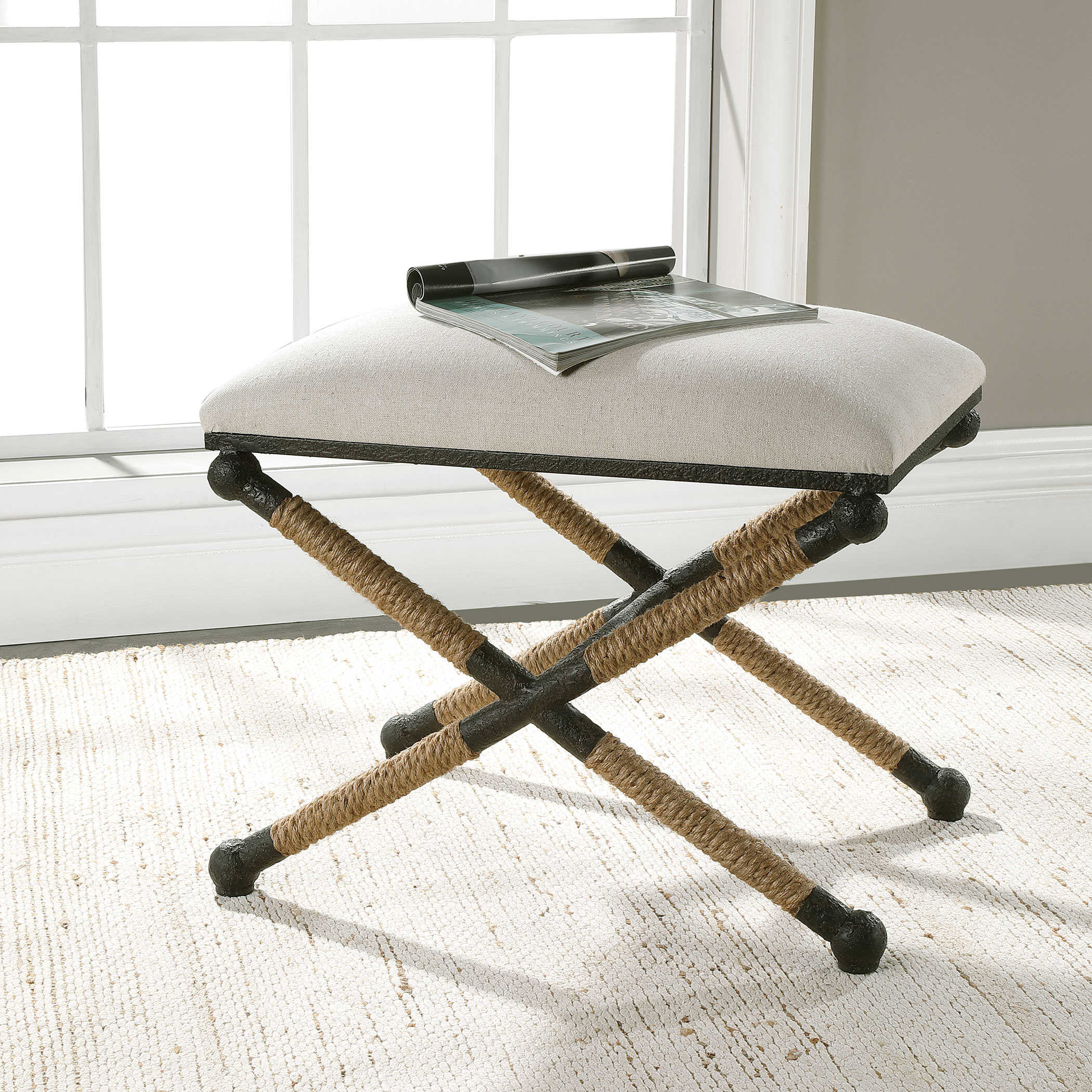 Small Backman Cotton Neutral Oatmeal X Rope Stool with Rustic Iron Frame, placed on a carpeted floor against a white wall.
