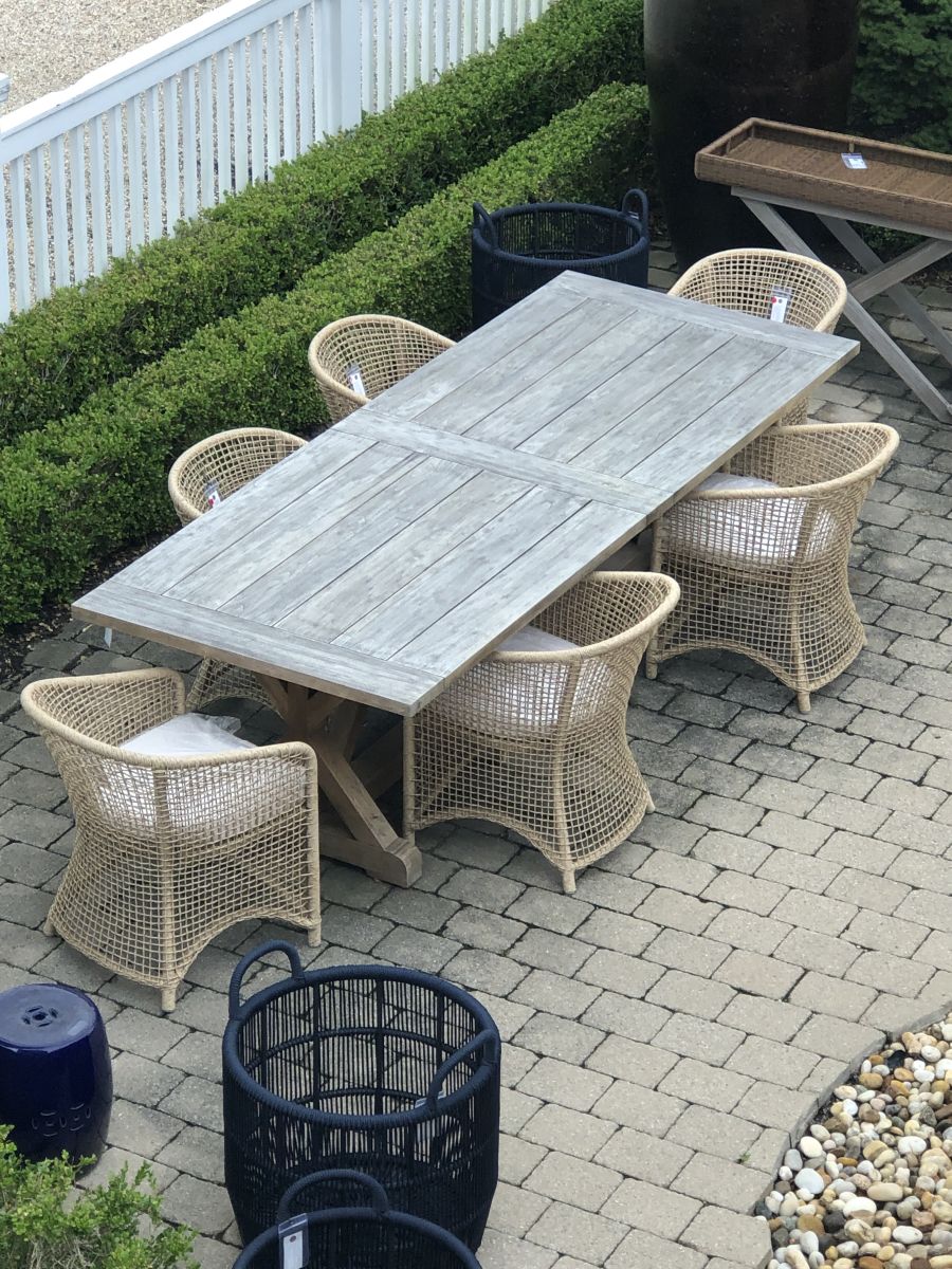 This image shows an outdoor dining set on a patio The table is surrounded by six wicker chairs with white cushions arranged