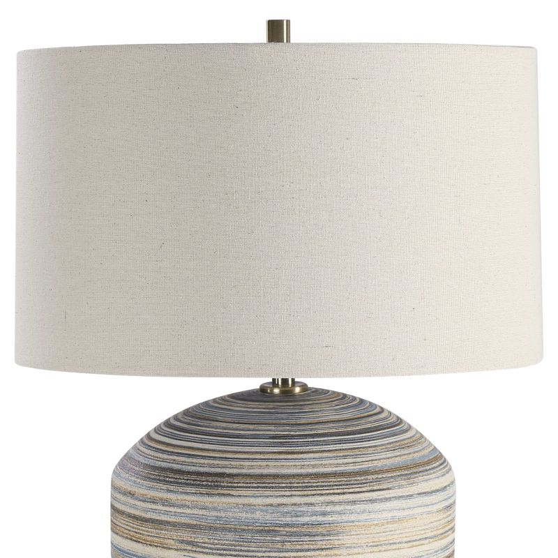 A striped brown and blue ceramic table lamp with a linen drum shade, featuring natural slubbing and brass hardware.