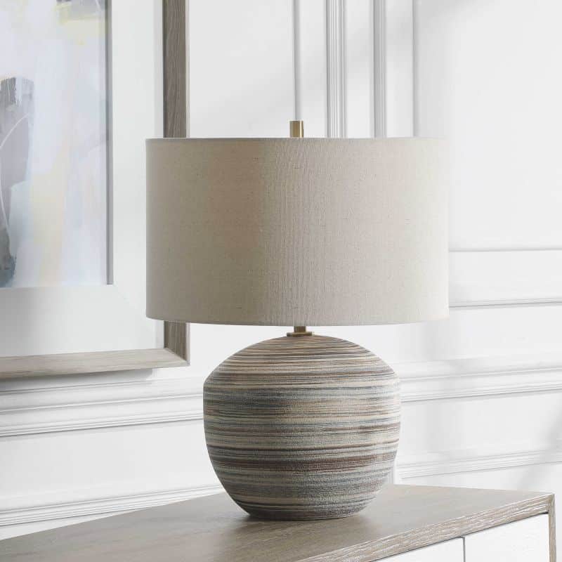 Luxurious ceramic table lamp with a striped brown, blue and cream linen shade that has natural slubbing and brass hardware.