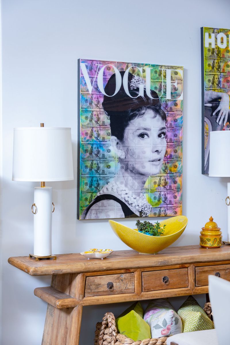 A framed image of a woman s face hangs on a wall above a table with colorful art pieces and a vase