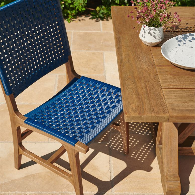This image shows a blue Hammond Side Chair with a woven design set against an outdoor table in a backyard setting The