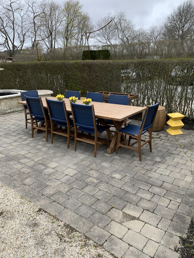 Outdoor dining area featuring a set of eight matching chairs with blue cushions, arranged around a dining table, on a brick patio.
