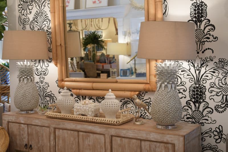 Large white pineapple lamp on display in a well-decorated interior space, featuring a decorative wallpaper and a stylish mirror above it.