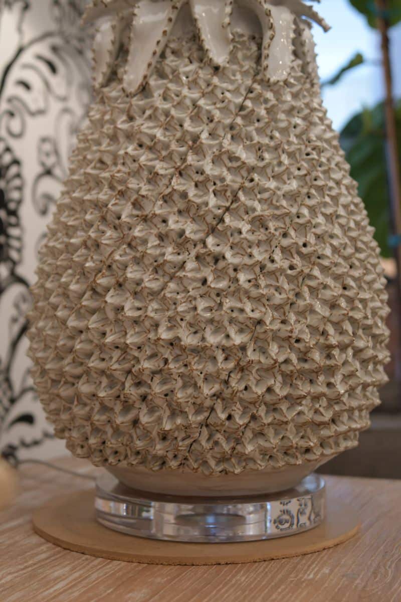 Large white pineapple table lamp with spiky texture, sitting on a wooden surface against a blurred background.