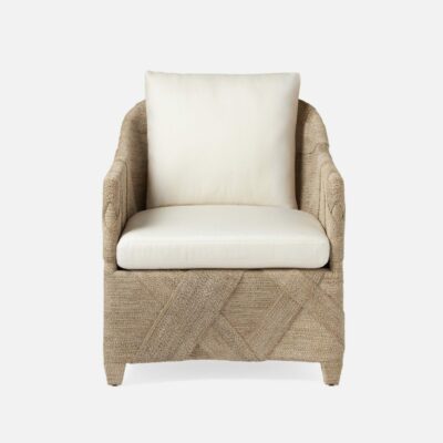 A stylish, wicker lounge chair with a white cushion in a bedroom setting.