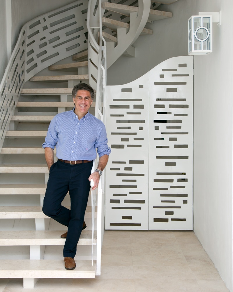 This image features a man standing at the bottom of a set of stairs wearing a blue shirt and dark pants The