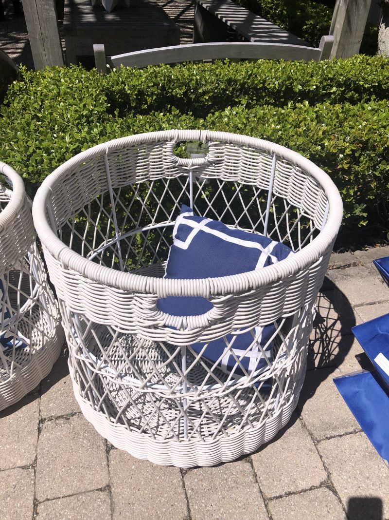 Large outdoor faux rattan basket, placed on brick patio next to wicker chairs.