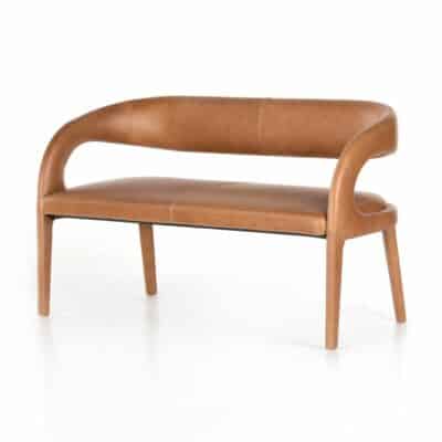 A sleek, modern leather bench featuring a curved design and a rich tan top grain finish, set against a plain white background.