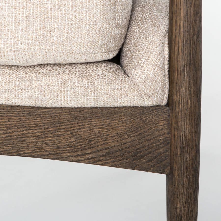 The image shows a modern wooden armchair upholstered in light camel fabric with a warm nettlewood oak frame It has a clean