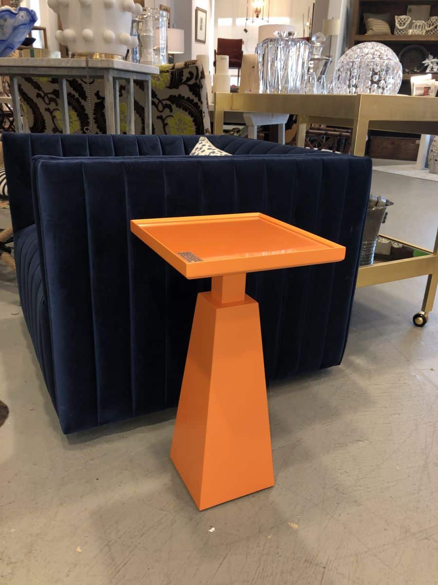Modern side table with glass top and blue velvet upholstered seat, set against a patterned wall.