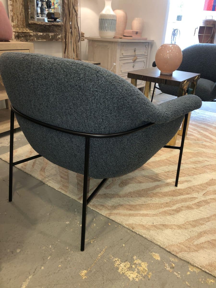 The image shows a mid-century style boucle chair in a living room setting, with its dark iron base on a patterned rug.