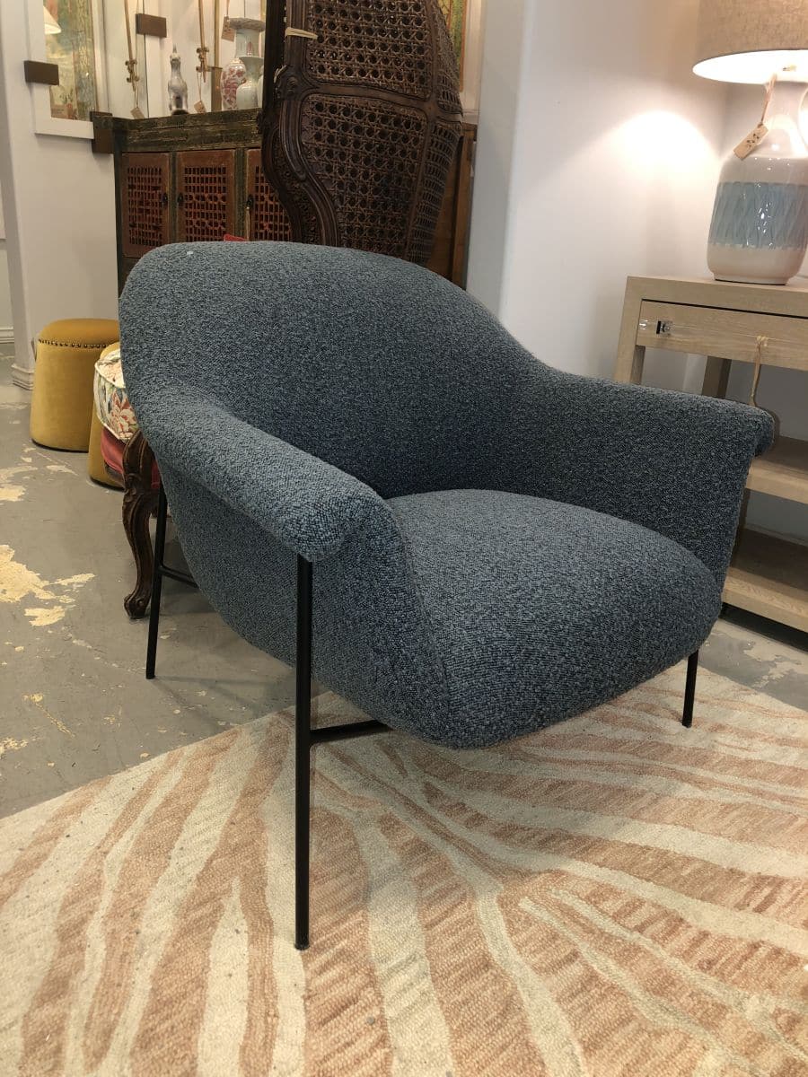 A stylish, blue boucle chair in mid-century design style with a black iron base, placed on a rugged surface.