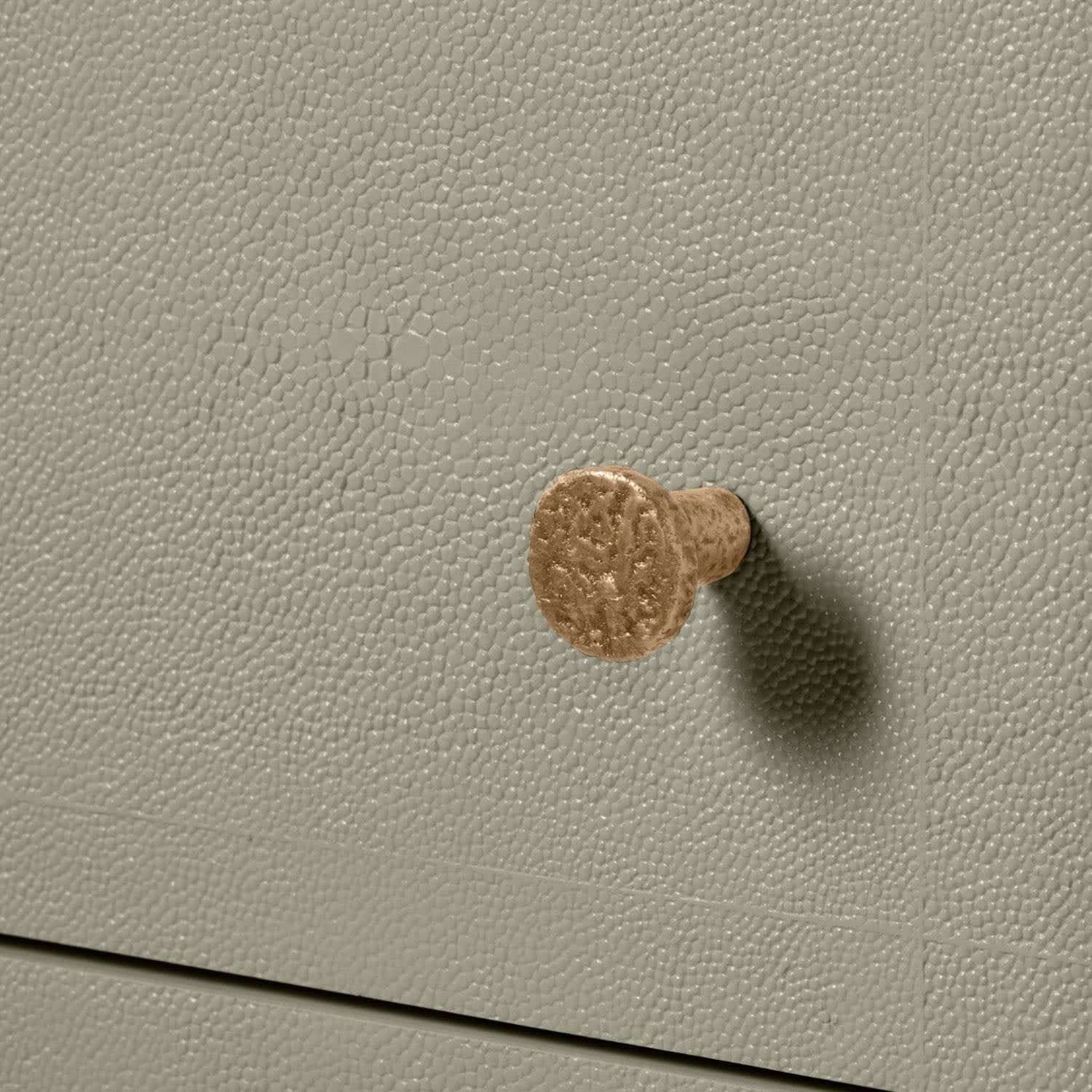 Small, round, metallic button attached to a beige surface.