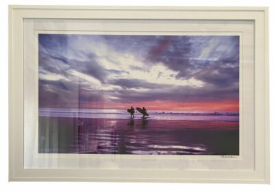 Surfer silhouetted against vibrant sunset, framed in double white matted photograph.