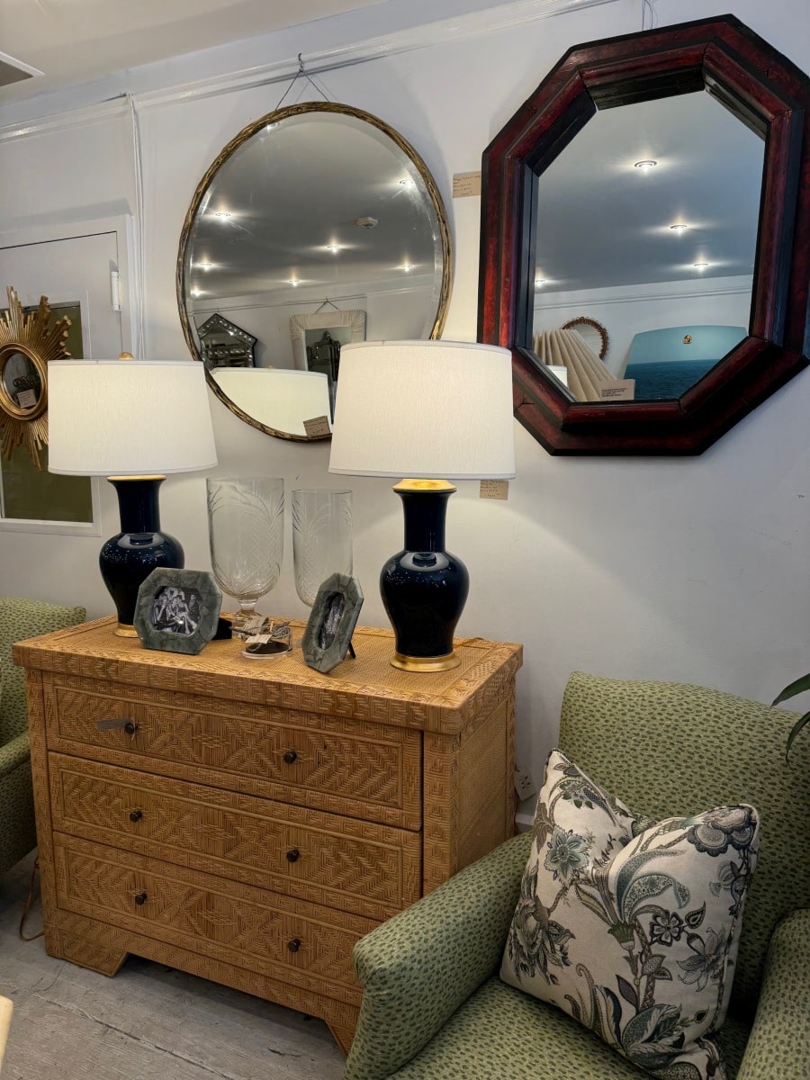 Round mirror with ornate frame, reflecting elegant lamp and decorative objects on wooden dresser.
