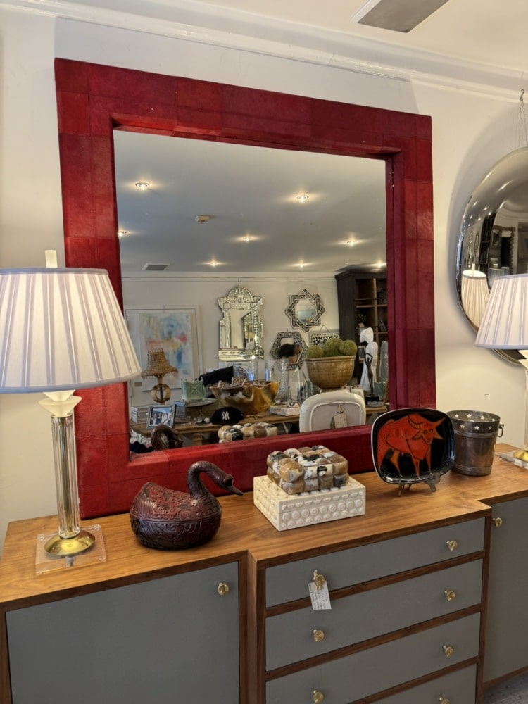 Close-up of Tauro Wall Mirror showcasing rich red hair on hide and double stitch detail against dark wood cabinet backdrop.