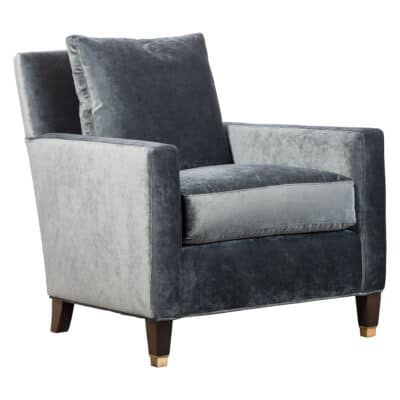 Close-up of blue velvet armchair with brass feet and pecan finish, showcasing comfort and elegance.