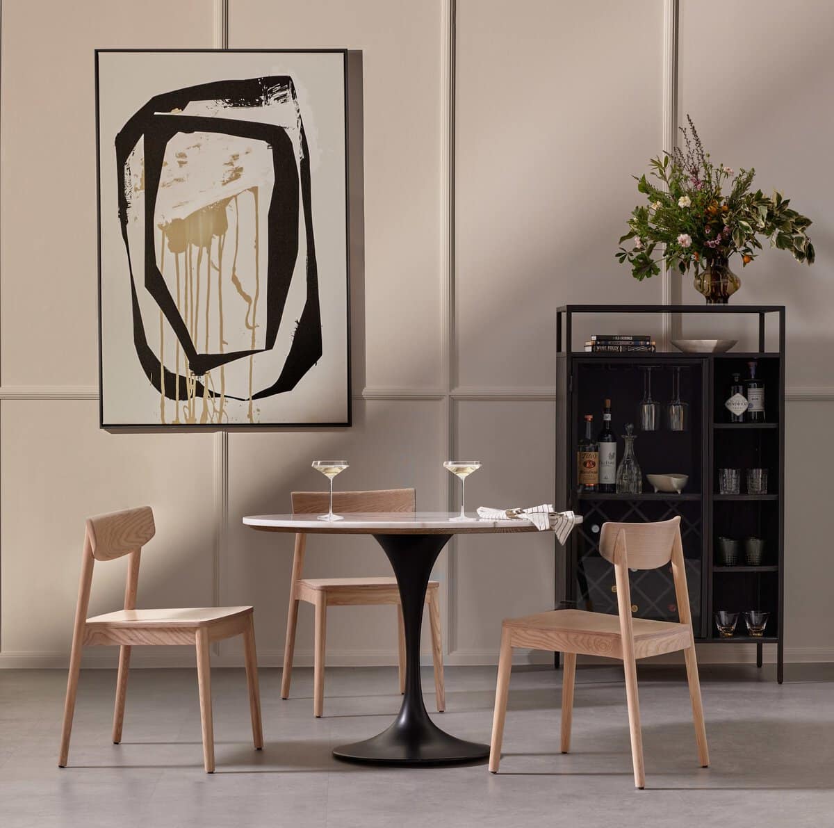 Stylish round dining table with marble top and tulip base, set against backdrop of modern art on wall.