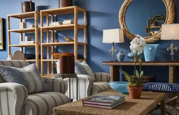 A cozy living room scene featuring Mecox-Collection furniture including plush blue and white armchairs against a vibrant blue wall backdrop with decorative