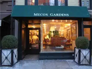 New York storefront with a green awning featuring the name Mecox Gardens on the second floor displaying various items in the window