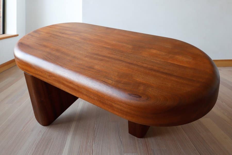 Handcrafted round coffee table with solid sapele wood finish, set against white wall in room.