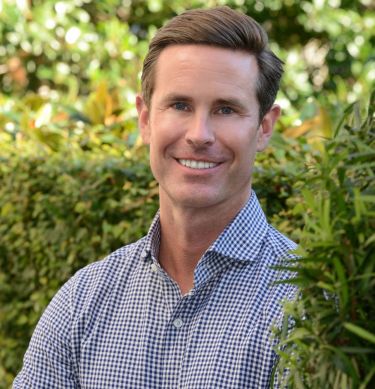Close-up of man wearing a blue plaid shirt, smiling at the camera.