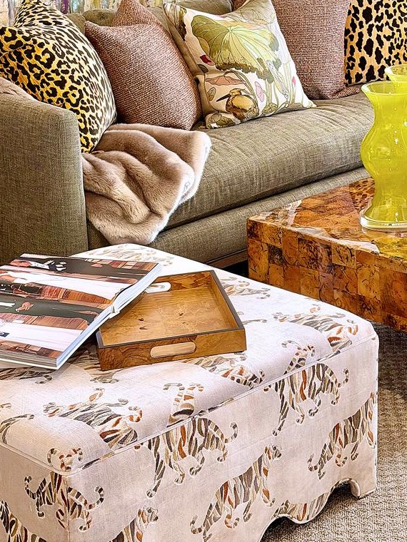 Mecox Gardens showroom vignette with leopard pillows, a burl wood coffee table and a tiger-print skirted ottoman