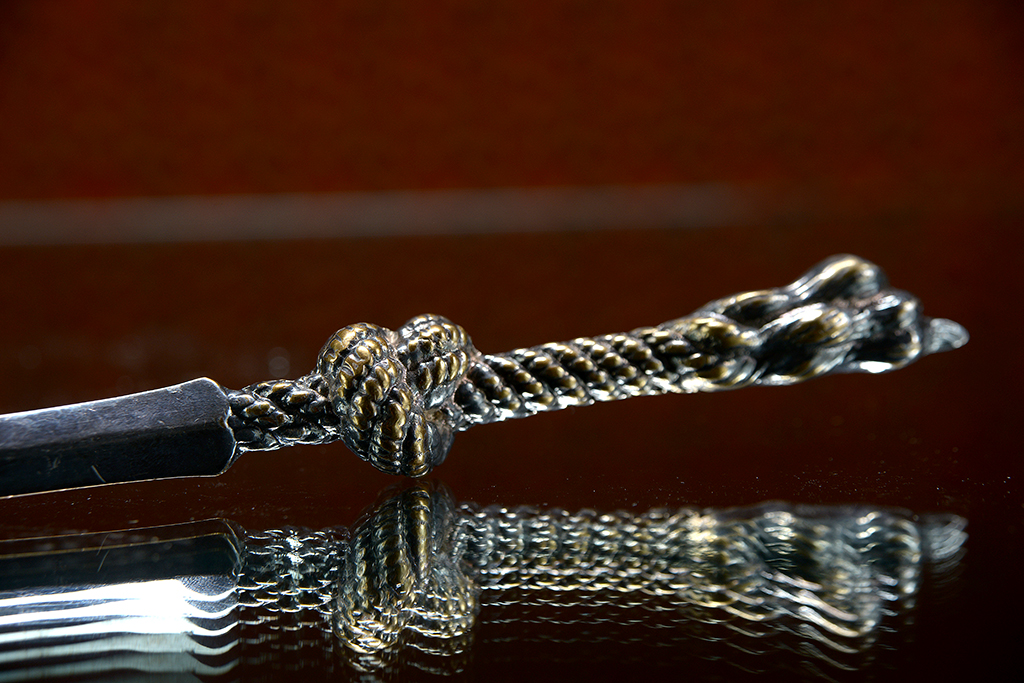 Vintage silver plated rope letter opener on a reflective surface