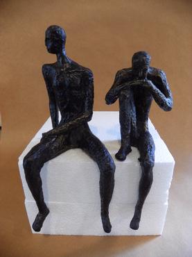 Two bronze metal sculptures of a man and a child on a white pedestal with the man in a thinking pose and