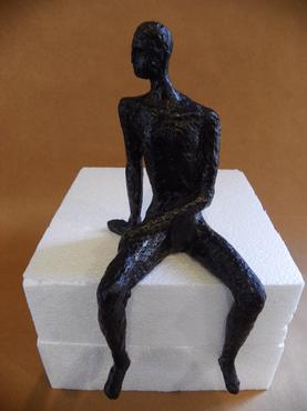 Bronzed metal sculpture of a man sitting on a white block with one hand resting on his knee and the other arm