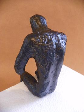 Bronze metal sculpture of a man in a thinking pose on a shelf with one hand resting on his knee and the