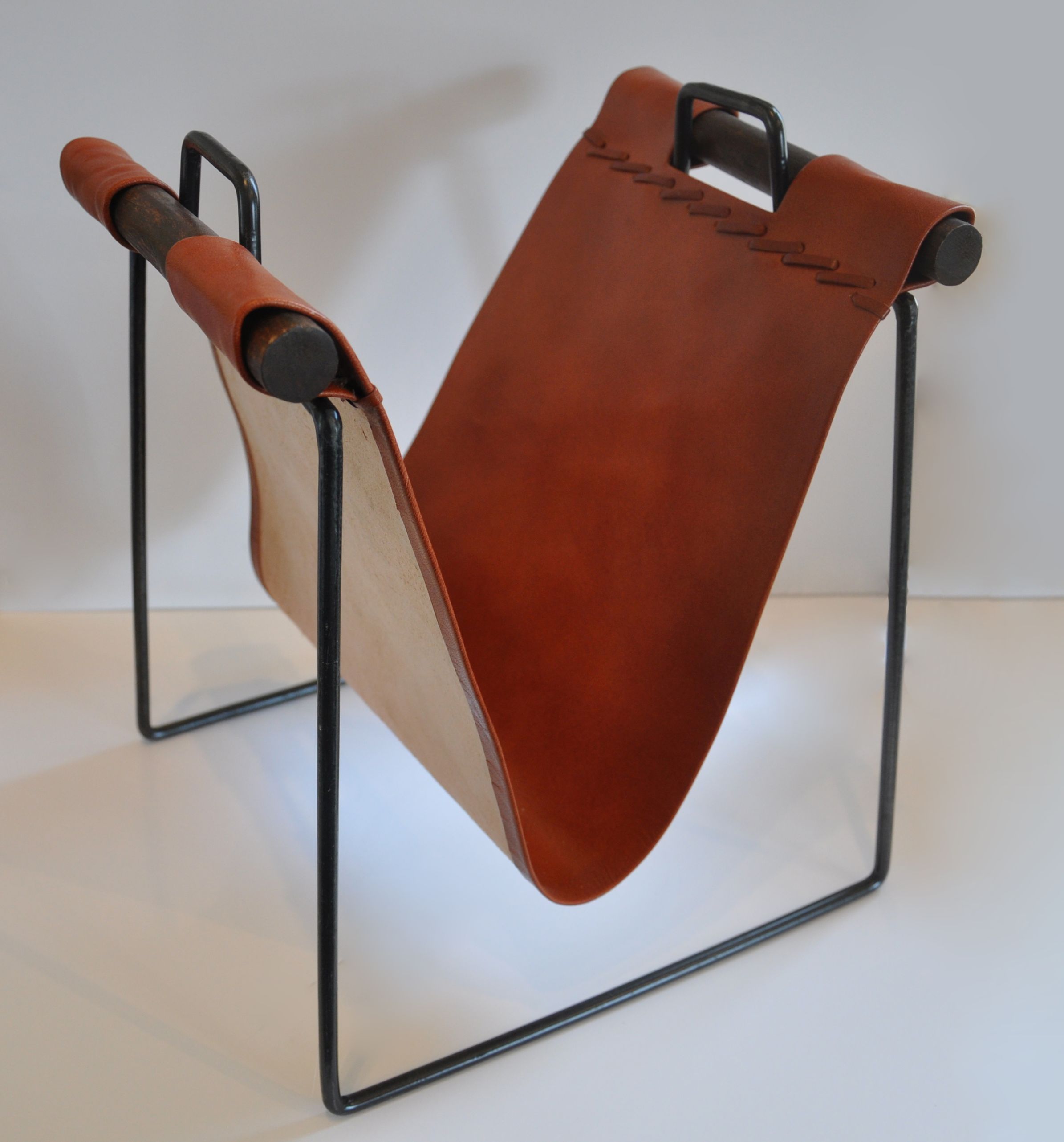 Iron and leather magazine rack with a brown leather seat, standing on a black metal stand against a white background.