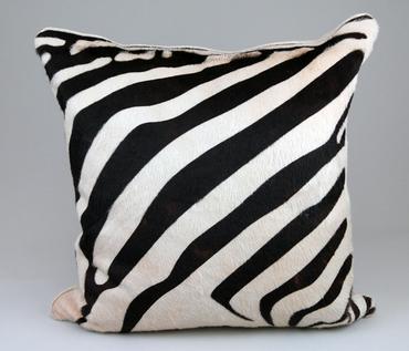 A large zebra embossed cowhide pillow with a flax color placed on a surface against a neutral background showcasing its pattern and