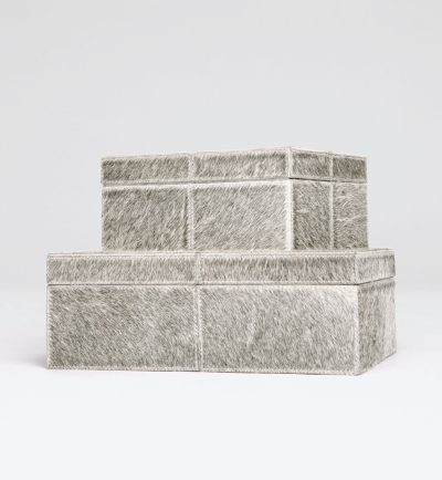 Grey cowhide boxes on a white background, one large and one small, with a focus on their texture and size difference.