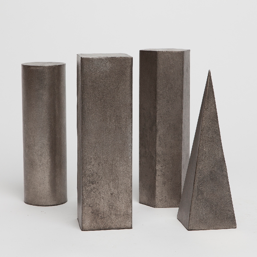 Three metallic sculptures and one smaller piece on a white background, with varying shapes including cylinders, prisms, and a pyramid.