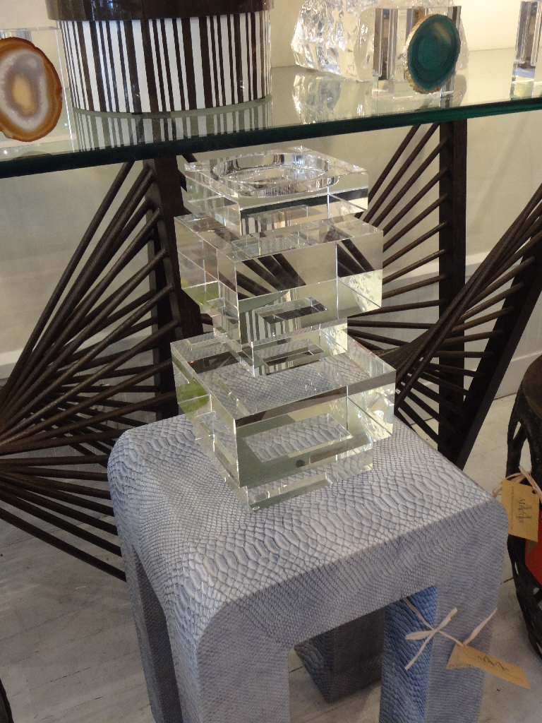 A display case with geometric crystal candleholders on a table one large and one small set against a backdrop of a wall
