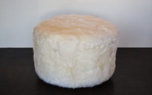 A round, fluffy Australian sheepskin ottoman with a metal decorative base.