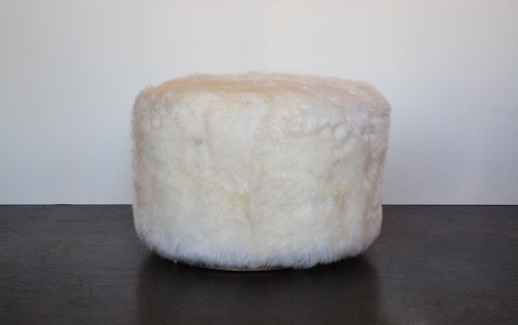 Circular ottoman with a plush, shaggy texture and a metal deco base.