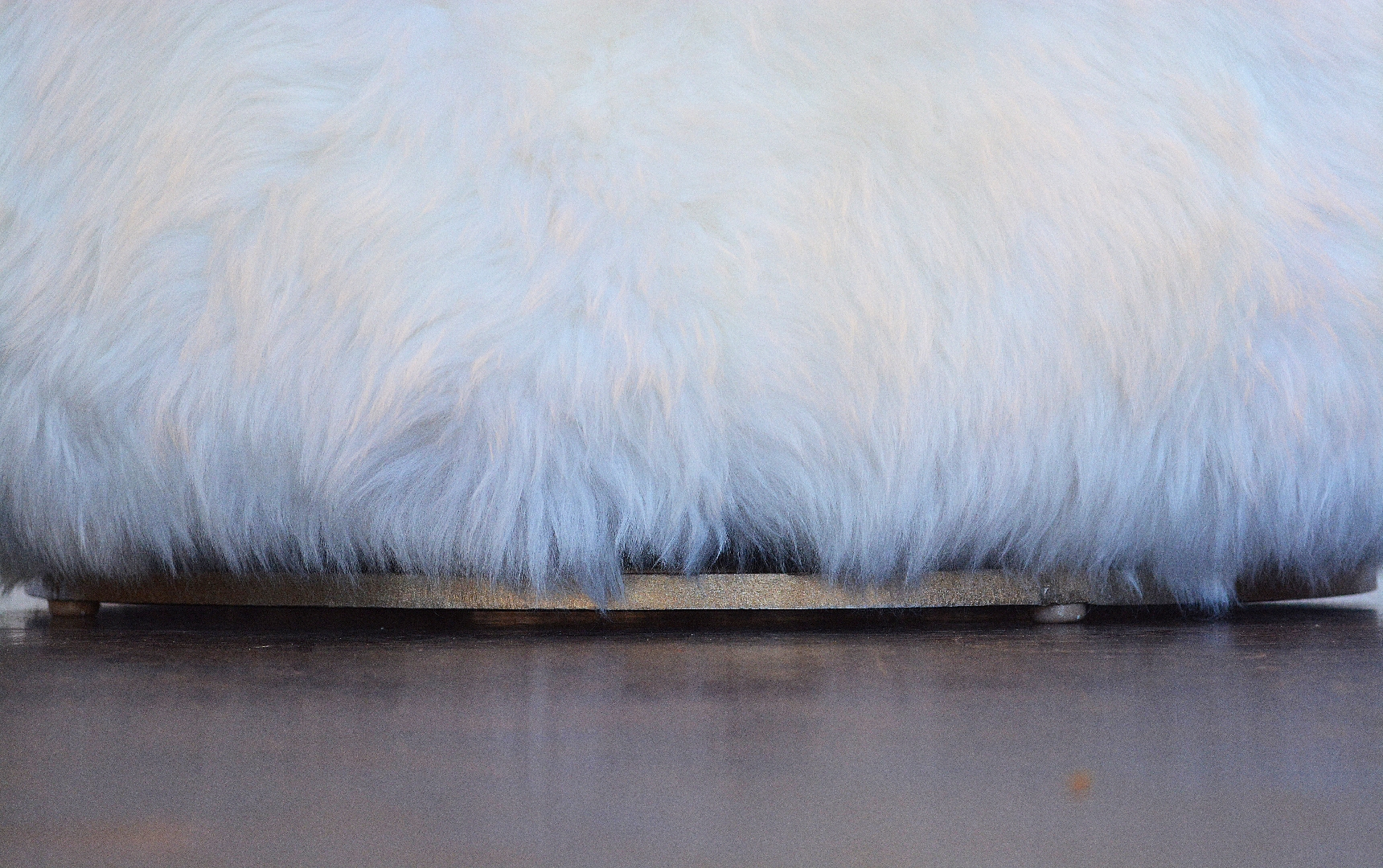 The image depicts a circular ottoman with a plush furry surface resembling an Australian sheepskin texture It features a metal decorative base