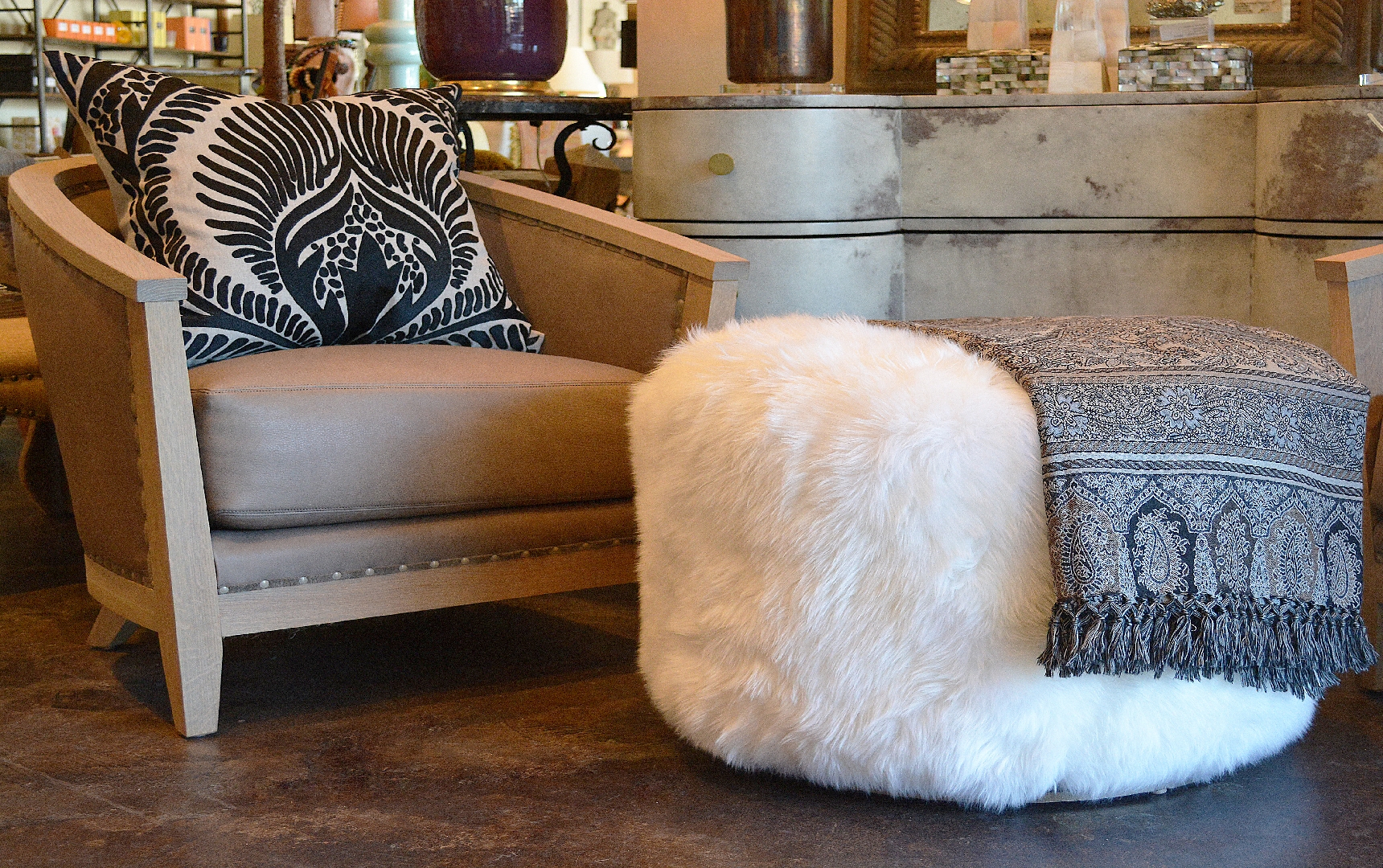 A circular ottoman with a metal deco base, topped with a large white fur throw.