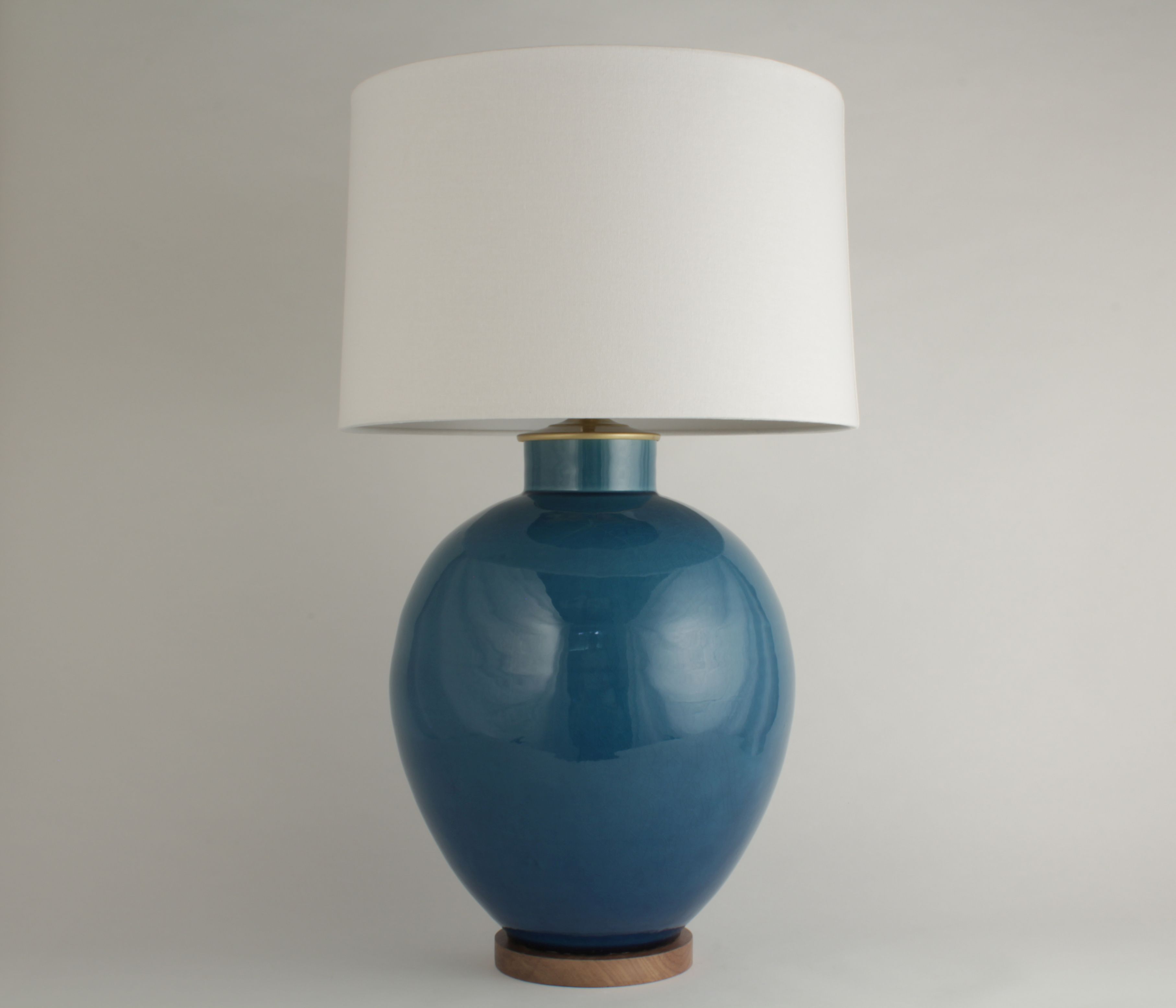 A tall, blue vase lamp with a white shade and a wooden base.