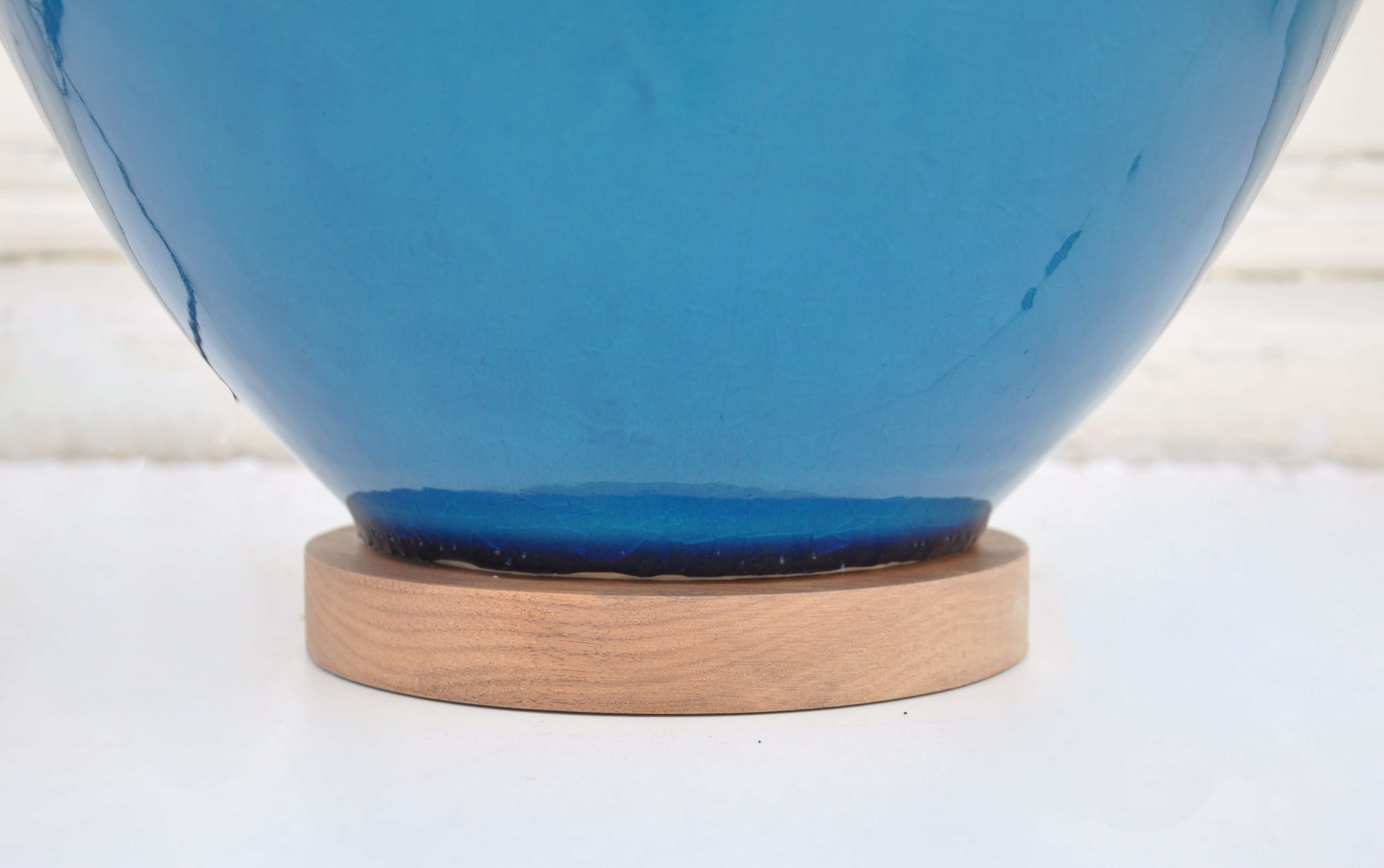 The image shows a blue ceramic lamp with a crackled finish placed on a wooden base It is a table lamp with