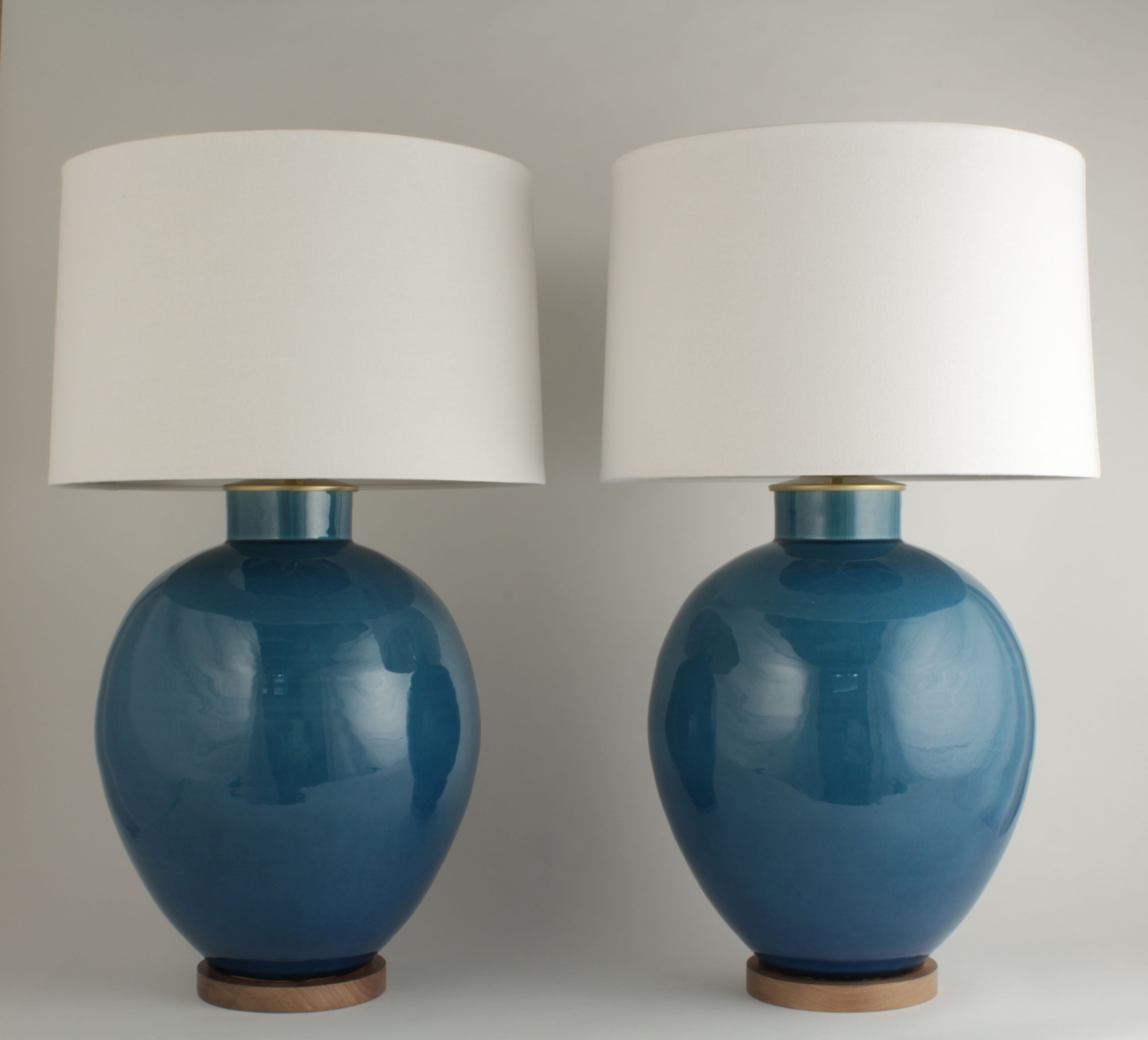Two ceramic table lamps with a glossy crackled teal finish each featuring a cylindrical body and a white shade on a wooden