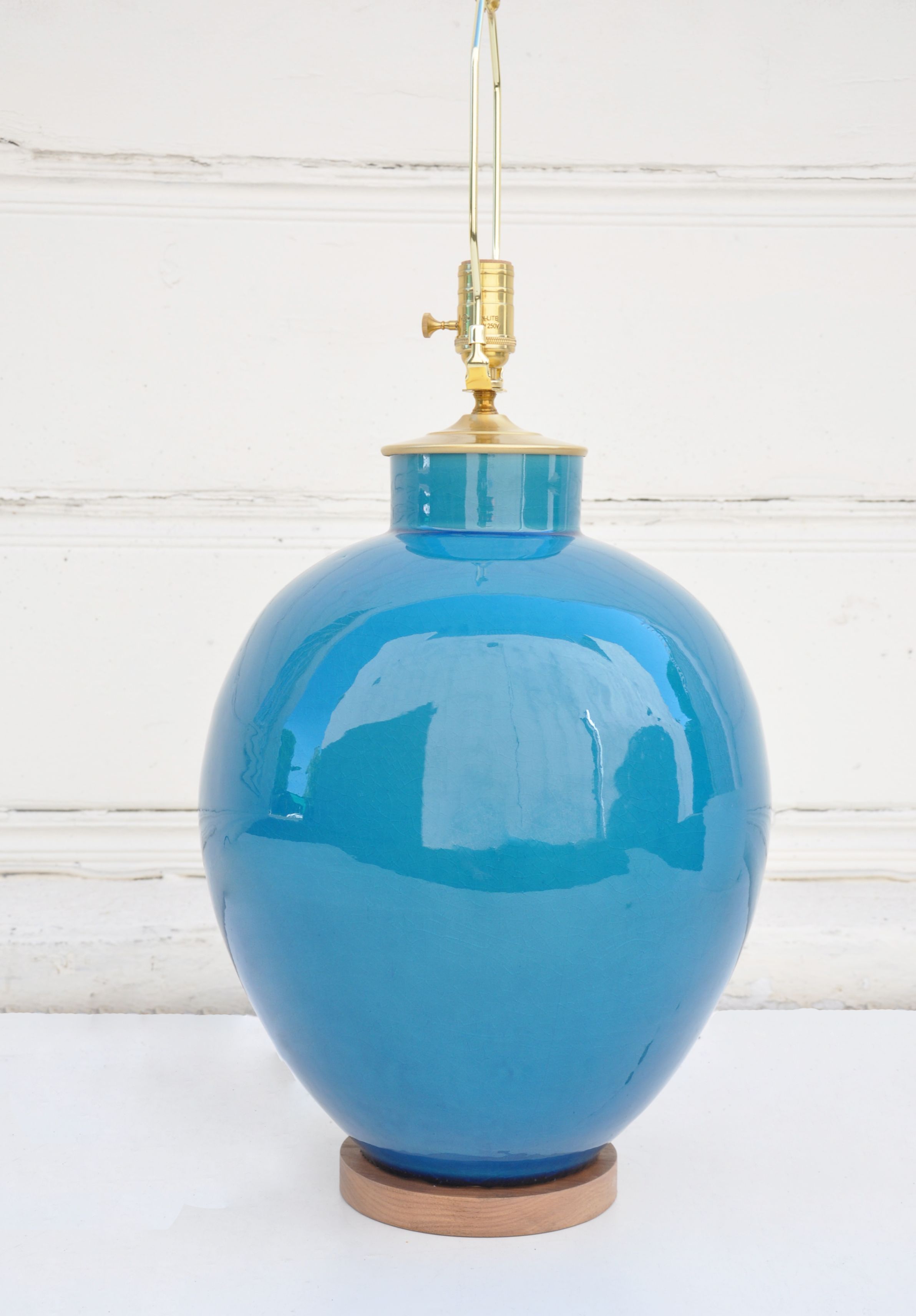 Blue ceramic lamp with a gold-toned base and a crackled teal finish, standing on a wooden surface against a white wall.