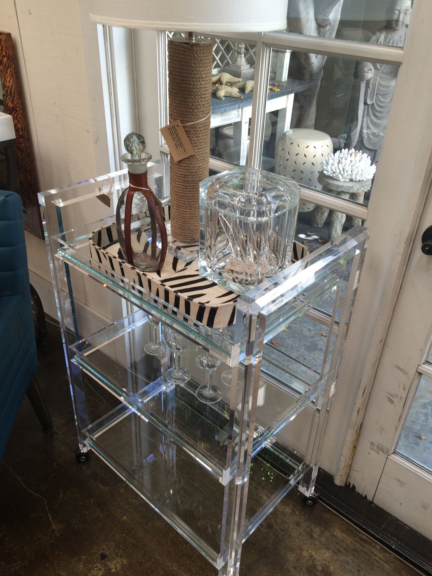 Glass and acrylic bar cart with three shelves, placed on a wooden floor.