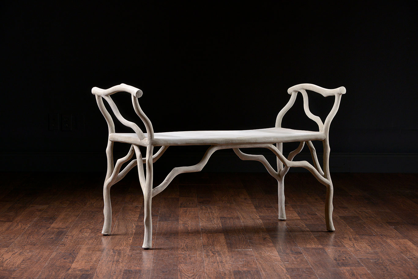 Faux bois concrete bench with curved backrest and twig details, set against dark background.