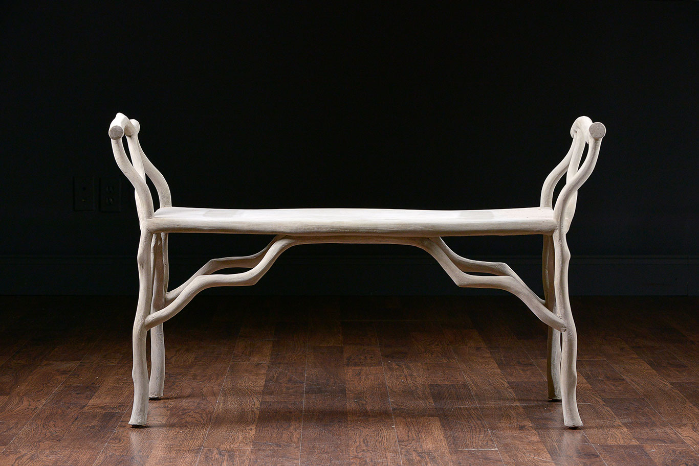 The image shows a faux bois concrete bench with a curved backrest and twig details placed on a wooden floor against a
