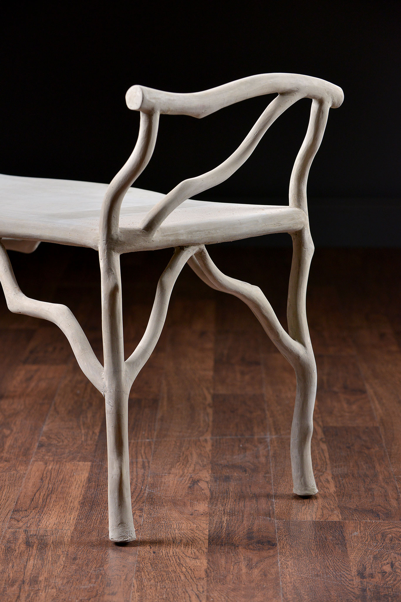 The image shows a faux bois concrete bench with twig details, positioned against a wooden backdrop.