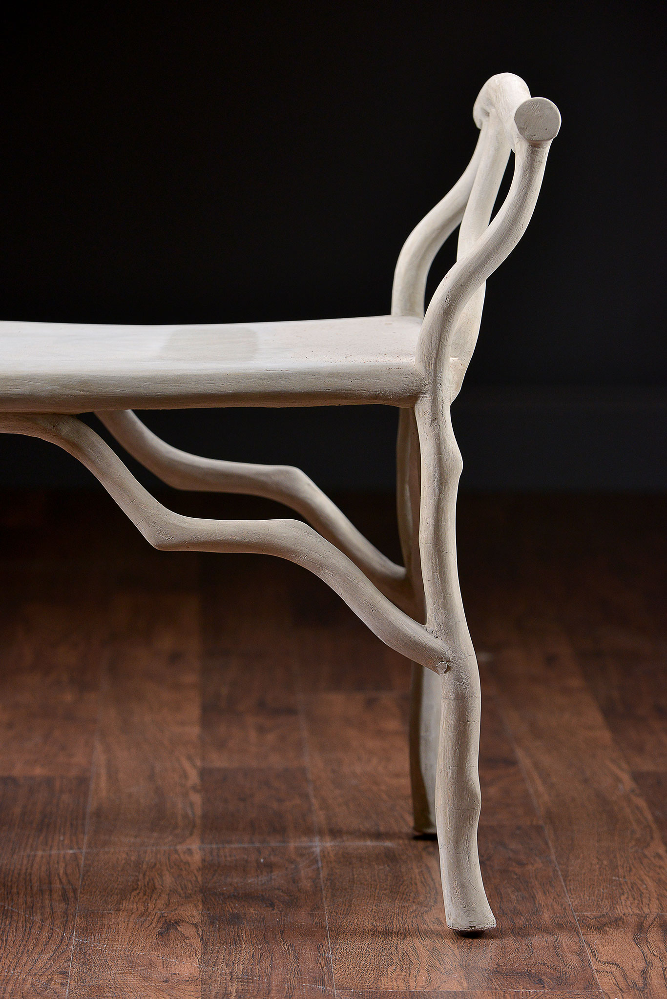 A wooden bench with curved armrests and a natural concrete finish, set against a dark background.